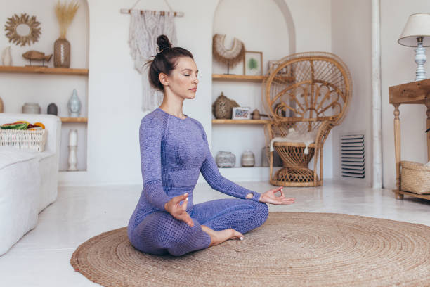 mulher sentada de pernas cruzadas com as mãos nos joelhos meditando, relaxando com o treino de ioga. - lotus position - fotografias e filmes do acervo