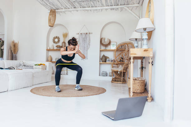 Woman working out at home doing squats with elastic band. stock photo