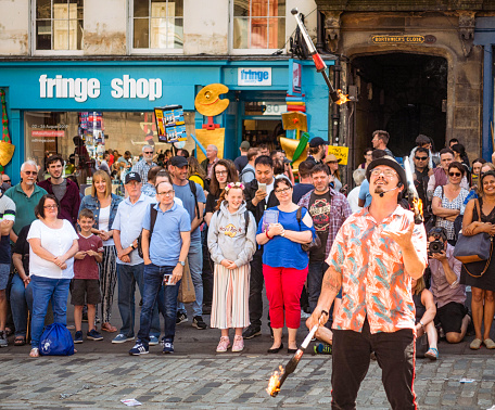 Edinburgh, Scotland - A street performer juggling with fire on the Royal Mile, watched by spectators outside the Edinburgh Festival Fringe Shop.