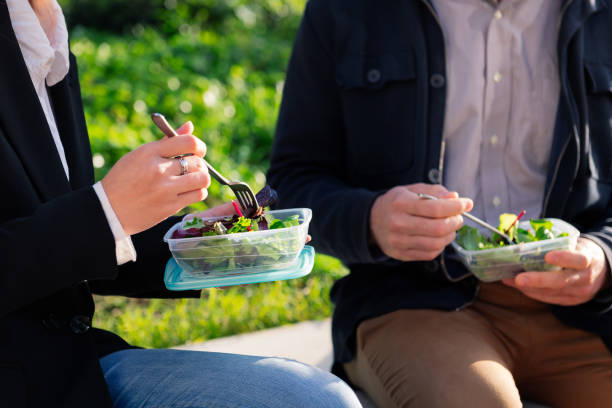manos de dos personas comiendo una ensalada en un parque - break office 30s 20s fotografías e imágenes de stock
