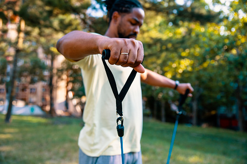 Man hand close up while exercise with Resistance Band outdoors. Afro American Male body workout using elastic bands in local park