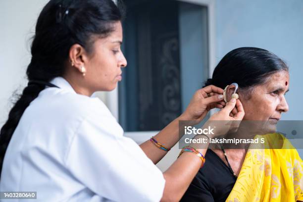 Happy Senior Woman Getting Fixed With Hearing Aid Machine From Doctor At Hospital Concept Of Elderly Impairment Expertise And Technology Stock Photo - Download Image Now