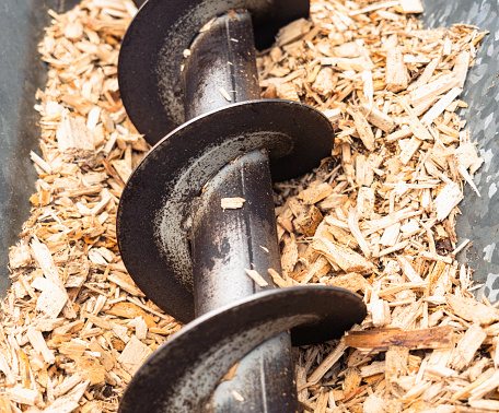 Close-up of wood chips in a hopper, ready to be moved into a boiler that burns biomass for sustainable heating.