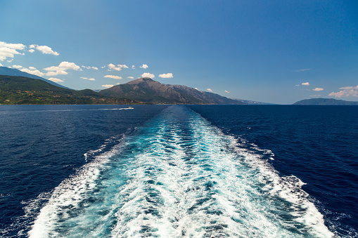 Bright sea water trail behind a cruise ship summer time. Ferry boat leaves a trail in a blue and clear water of Mediterranean Sea leaving Cephalonia island, Greece.