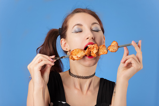beautiful woman eats grilled meat on blue background