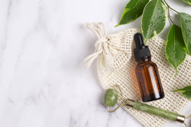 istock Unbranded serum bottle, face roller with leaves on marble background. Jade face roller for facial massage therapy. Anti age, lifting and toning treatment 1403291532