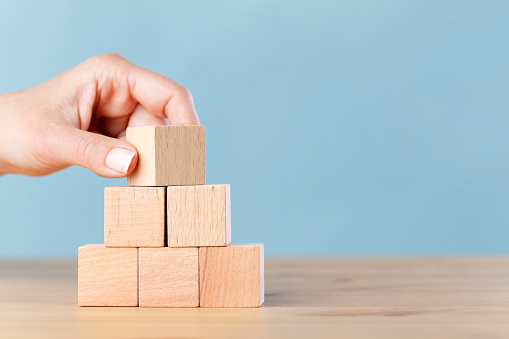 Woman hand flips blank wooden cube on top pyramid, place your own creative success symbols