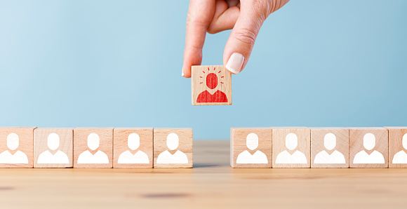 Person icon on wooden cube with hand picked different from the crowd