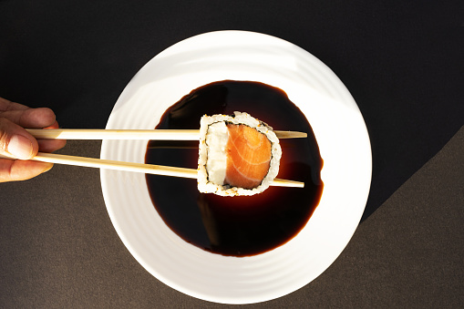 Maki held with chopsticks on top of a plate with soy sauce