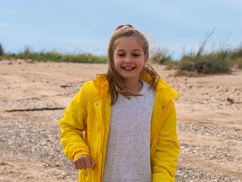 A beautiful smiling blonde teenage girl in a yellow jacket walks along the sandy seashore. Freedom and a healthy lifestyle spring-summer concept. A happy girl is traveling.