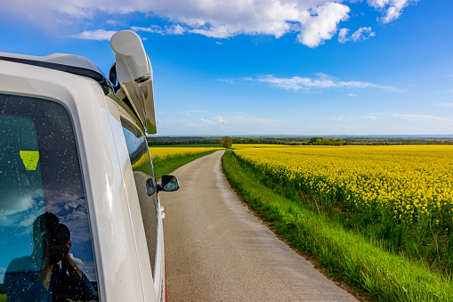 Cropped image of white van moving on country road amidst rapeseed field against blue sky
