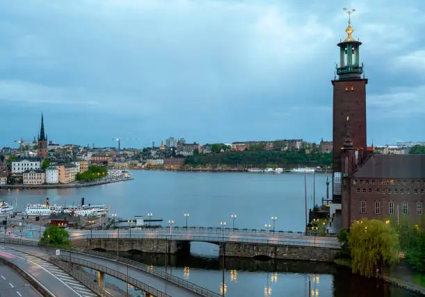 panoramic view across the water area Riddarfjärden onto the districts Riddarholm and Södermalm of Stockholm with the tower of the Stadshuset on the right edge at nightfall, Sweden