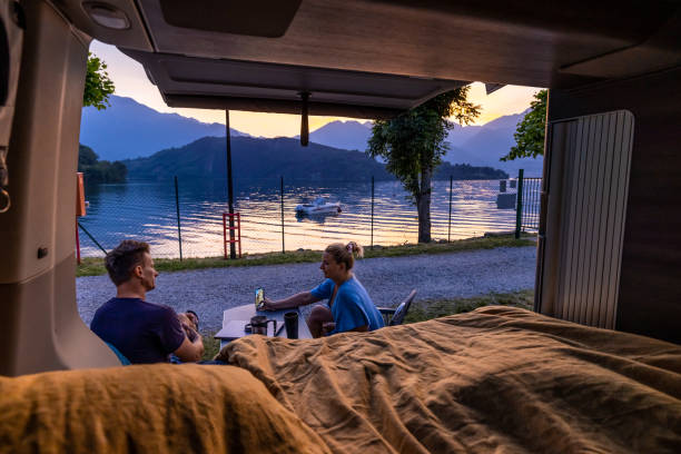 istock Couple sitting on chairs watching mobile phone beside camper van by Lake Como 1403296714