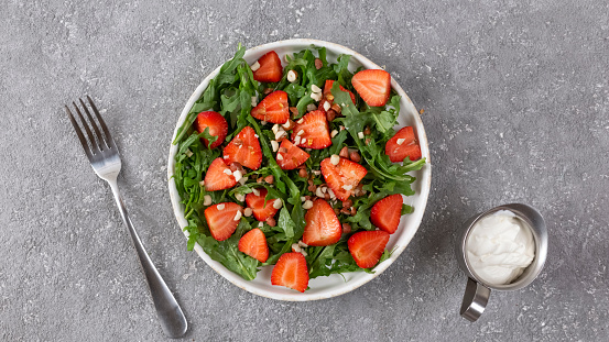 Delicious salad of arugula and strawberries on a white dish, healthy food, top view