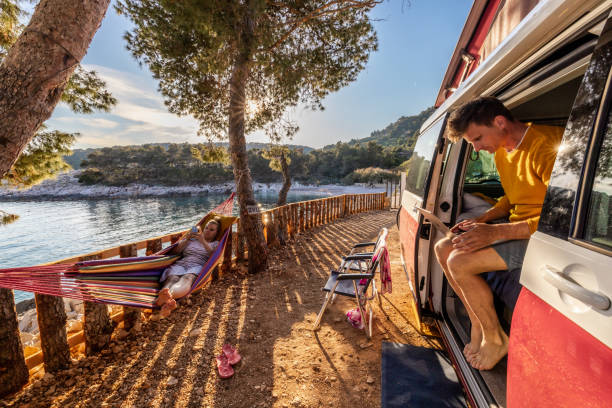 istock Couple using mobile phone and laptop while camping beside sea 1403297430