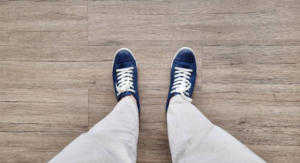 feet in denim sneakers standing on wooden vinyl floor, selective focus. fashion hipster cool man with wblue sneakers and beige pants, soft vintage toned colors for beginning concept. feet in denim sneakers standing on wooden vinyl floor, selective focus. fashion hipster cool man with wblue sneakers and beige pants, soft vintage toned colors for beginning concept. running shoes on floor stock pictures, royalty-free photos & images