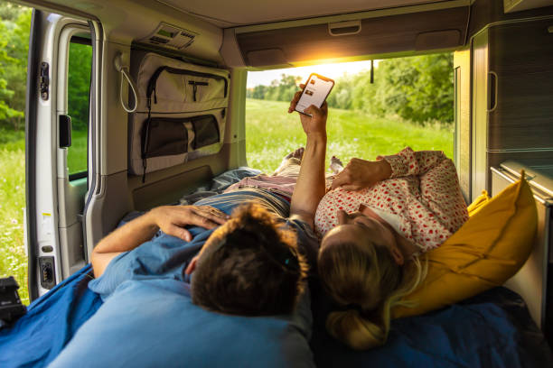istock Mid adult couple using mobile phone while lying on bed inside van 1403302045