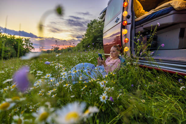 istock Carefree woman using smart phone while resting on field against campervan during sunset 1403302226