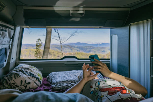 istock Carefree woman using mobile phone while relaxing on bed in camper van 1403302986