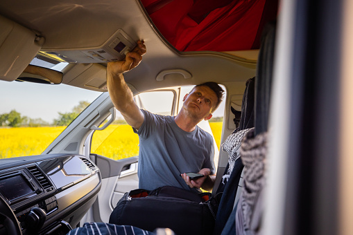 Man with short brown hair standing at his van,pressing a button in the cockpit of the van to extend the roof,van life