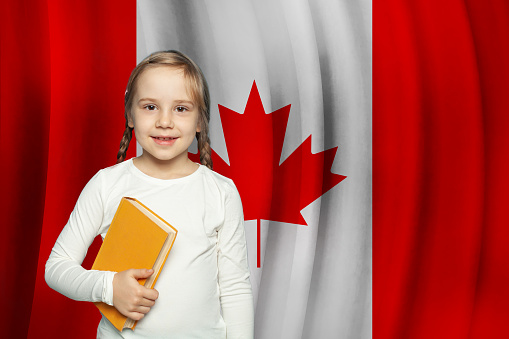 Cheerful little kid child girl with book on flag of Canada background. Education in Canada concept