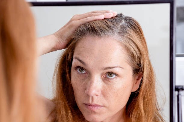 mujer de pelo gris mirando el reflejo en morror - women middle aging process covering fotografías e imágenes de stock