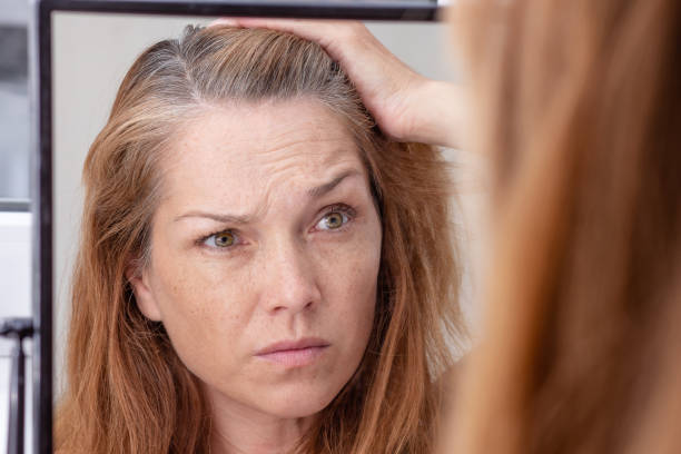 mujer de pelo gris mirando el reflejo en morror - women middle aging process covering fotografías e imágenes de stock
