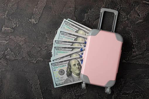 Travel.Vacation money saving concept,beach vacation.Miniature luggage and bundles of hundred dollar bills.Vacations.Copy space.Savings concept for vacation.