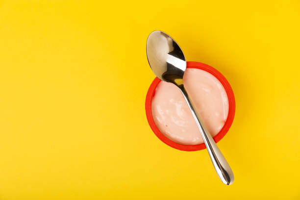 istock Delicious berry yogurt with a small spoon. Composition with plastic cups for yogurt on a yellow paper background. Healthy food. Proper nutrition. Place to copy. Place for text. Top view. 1403309898