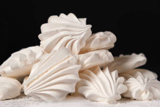 istock Airy sweet meringue on powdered sugar on a black background close-up, side view. 1403314620