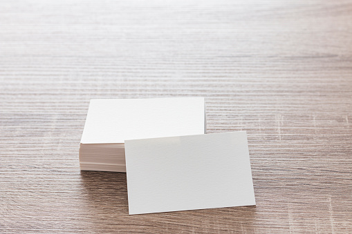 On a table is a stack of blank textured cardboard business cards. One of them is leaning on the stack facing the frame.