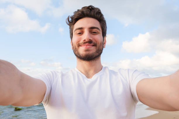 Happy man taking selfie using mobile phone at beach on outdoor stock photo