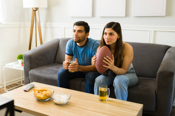 hispanic sports fans watching american football on the sofa - american football football food snack imagens e fotografias de stock