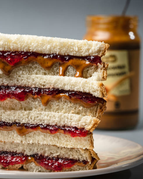 stack of peanut butter and strawberry jelly sandwich and jar of peanut butter out of focus in background stack of peanut butter and strawberry jelly sandwich and jar of peanut butter out of focus in background peanut butter and jelly sandwich stock pictures, royalty-free photos & images