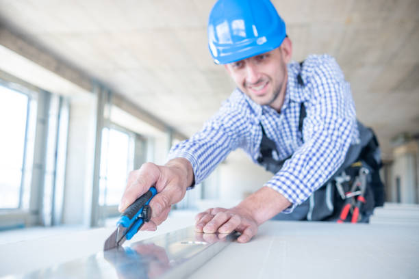 A cheerful construction worker cuts drywall with a utility knife.