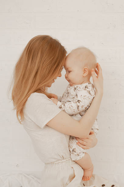 retrato de la joven madre feliz sosteniendo a un pequeño y lindo bebé regordete, tocándose con cabezas sobre fondo blanco. - vertical caucasian glasses red hair fotografías e imágenes de stock