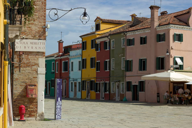 Venice, Italy: Island of Burano, the center of the cathedral square Venice, Italy - September 03, 2018: Island of Burano, the center of the cathedral square and colorful facades of the corner building and several houses, narrow to each other venice italy grand canal honeymoon gondola stock pictures, royalty-free photos & images