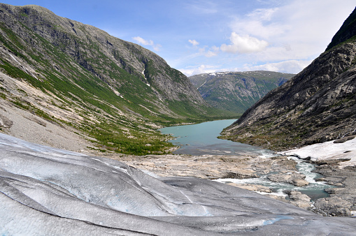 A large glacier in a valley between mountains in the north of Europe in Norway. Frozen snow in the mountains in summer.