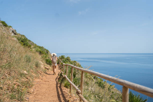 istock Young woman wearing hat and backpack walks above sea, 1403335971