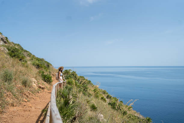istock Young woman wearing hat and backpack walks above sea, 1403335977