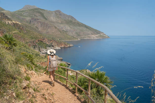 istock Young woman wearing hat and backpack walks above sea, 1403336022