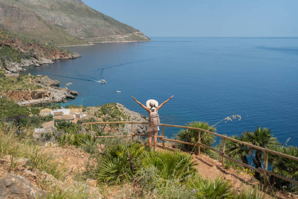 istock Young woman wearing hat and backpack walks above sea, 1403336029