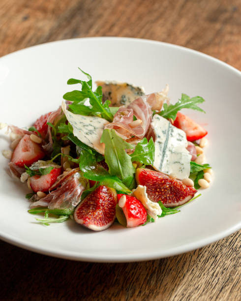 Prosciutto di Parma salad with figs and blue cheese Salad with hamon ham, figs, blue cheese, arugula and strawberry on a plate. Dark Wooden background. plate fig blue cheese cheese stock pictures, royalty-free photos & images