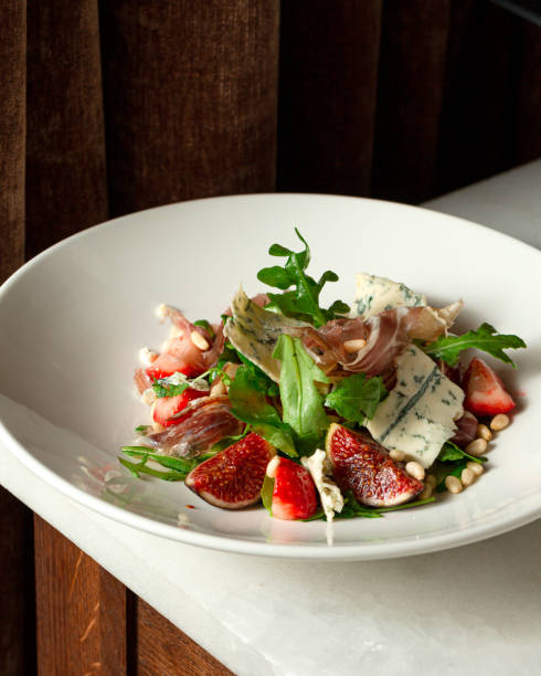 Salad with hamon ham, figs, blue cheese, arugula and strawberry on a plate. Dark Wooden background.