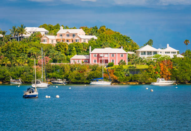 Hillside Community Sailboats and small motor boats float in the shallow water in a bay in front of large, stately  homes that are  nestled in the steep but low hills above the water line on the outskirts of Hamilton, Bermuda. bermuda stock pictures, royalty-free photos & images