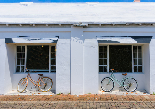 Two bicycles are parked in the alcove of a white washed building in front of shop windows.