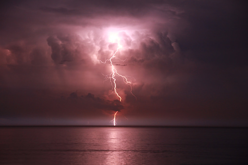 Evening thunder storm over the ocean coast with electric lightning strike over the water on the horizon