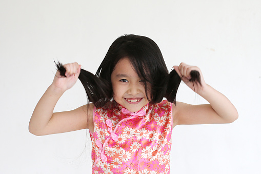 Portrait of an Asian girl grabbing her hair while smiling joyfully.