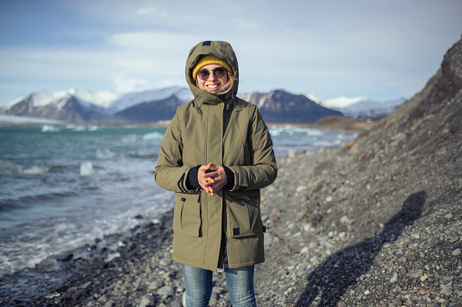 A millennial woman stands not far from a glacial lake and looks directly into the camera. ISL