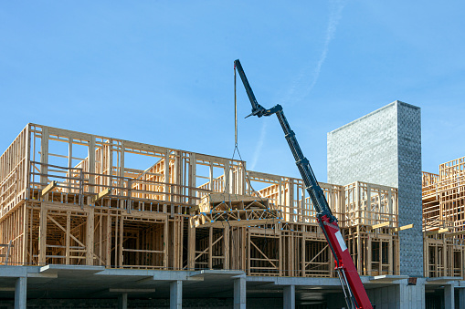 Photo of project manager visiting construction site with Multi-Ethnic construction workers standing on roof top at sunset. Business, building, industry, technology and people concept - smiling builder in hardhat with blueprint over group of builders at construction site under the tower crane.